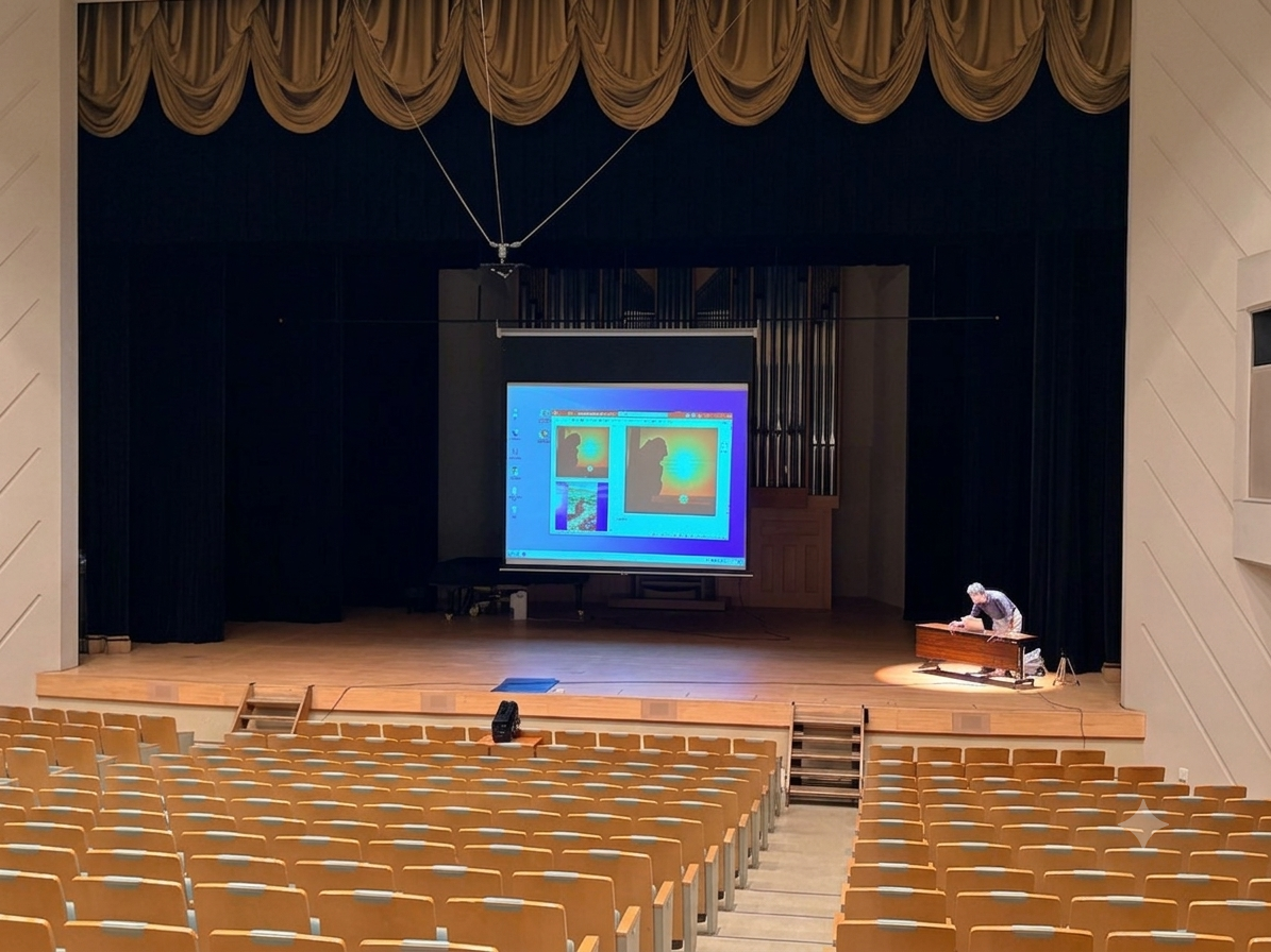 中新田バッハホールのステージにて、巨大なパイプオルガンとスクリーンを背景に講演のリハーサルを行う佐藤誠悦さん。空席の客席から見た引きの構図。
